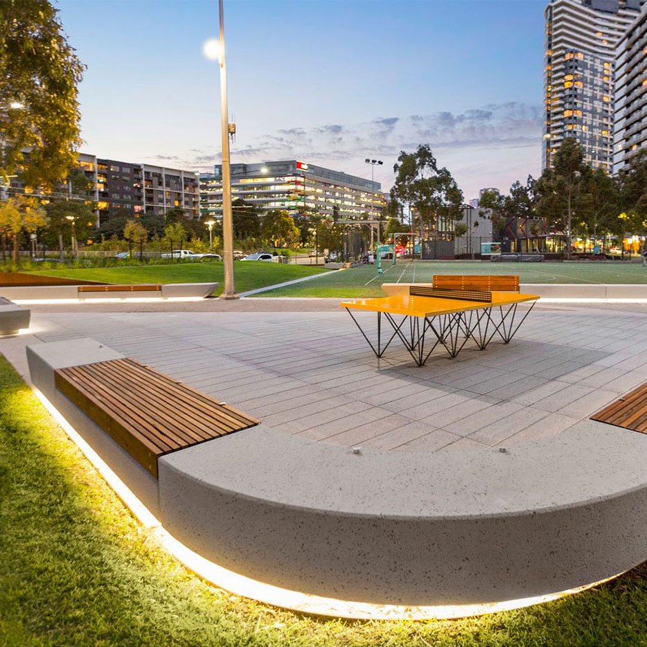 Outdoor ping pong table with benches in a park setting with buildings in the background